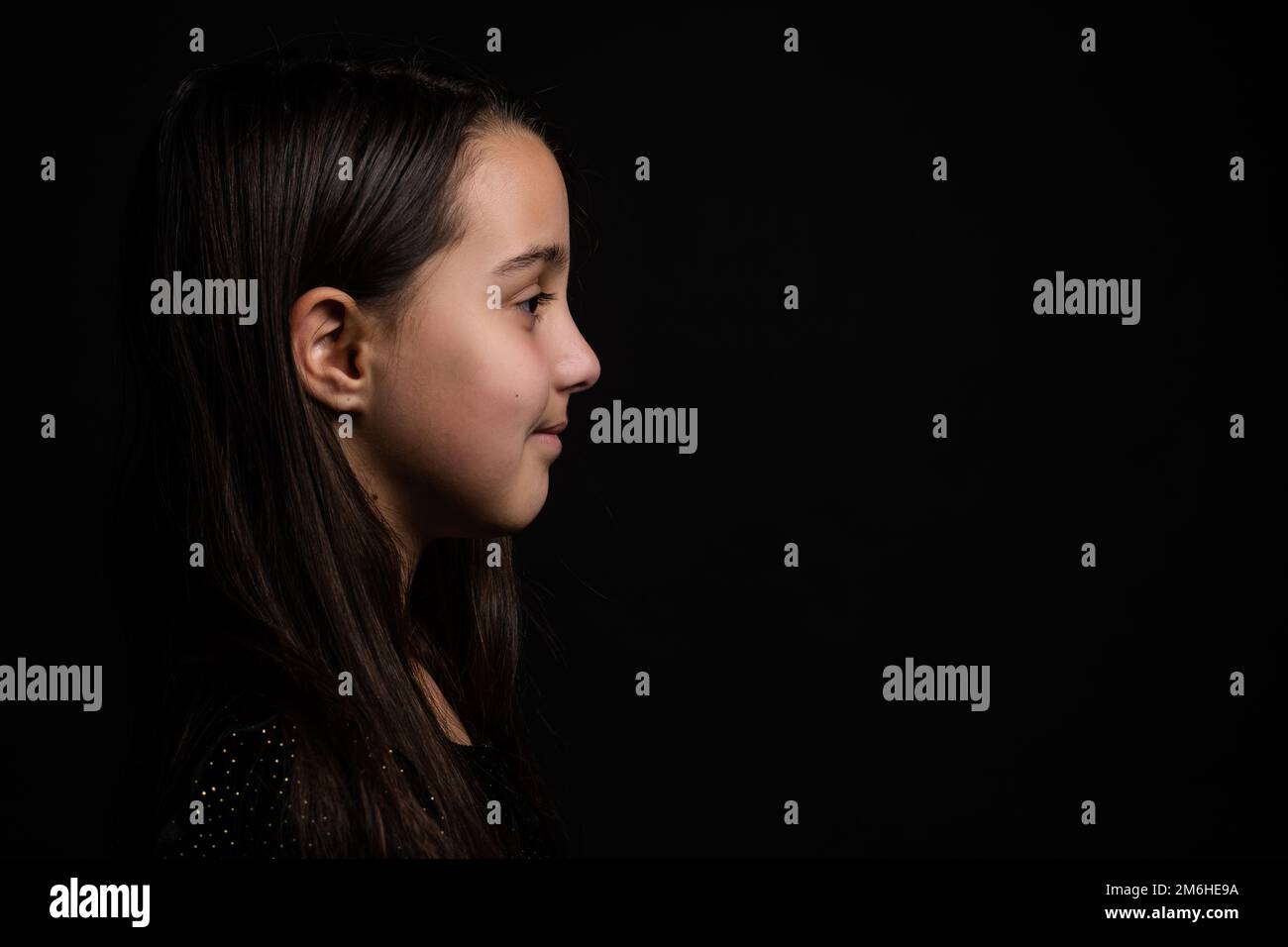 Profilo vista laterale faccia bambina dai capelli castani in piedi isolata su sfondo nero studio Foto Stock