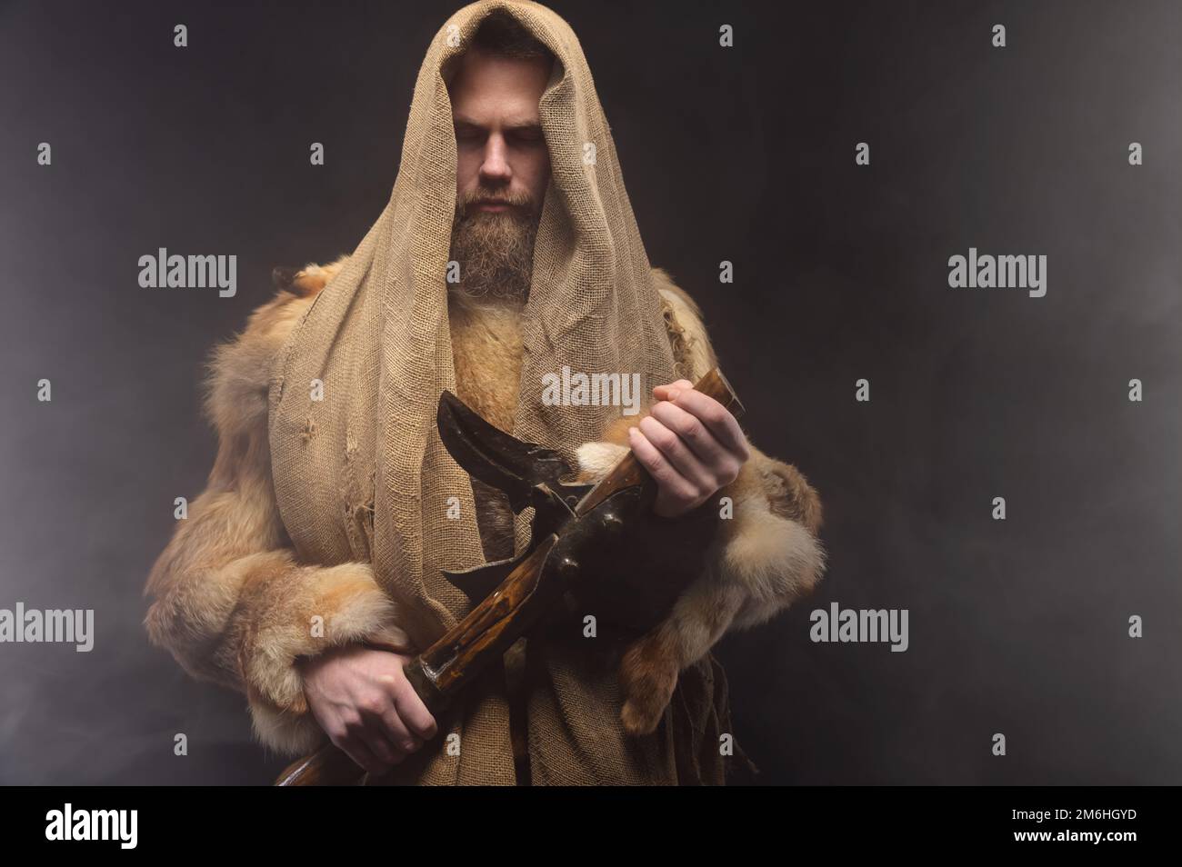 Ritratto di un guerriero scandinavo in abiti antichi di pelliccia e tela. Si trova nello studio circondato da fumo con un A. Foto Stock