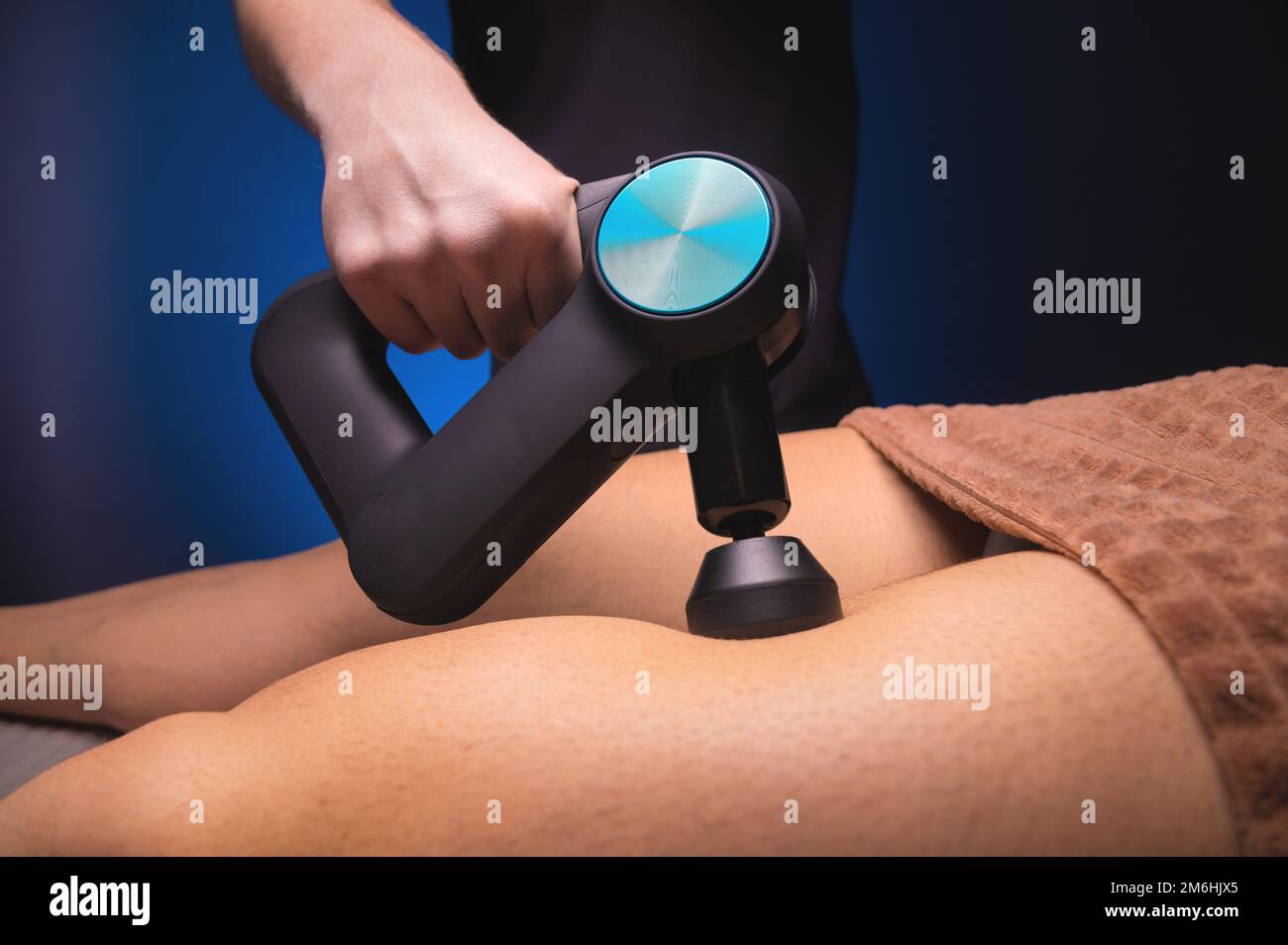 Il primo piano di un massaggiatore professionale maschile stimola i muscoli delle gambe di un paziente maschile in una sala termale scura per il massaggio. Percussione Foto Stock