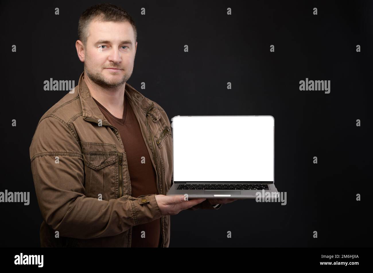 Attraente positivo amichevole maschio caucasico tenendo in mano il computer portatile che presenta il suo schermo tagliato con spazio copia sul dorso nero Foto Stock