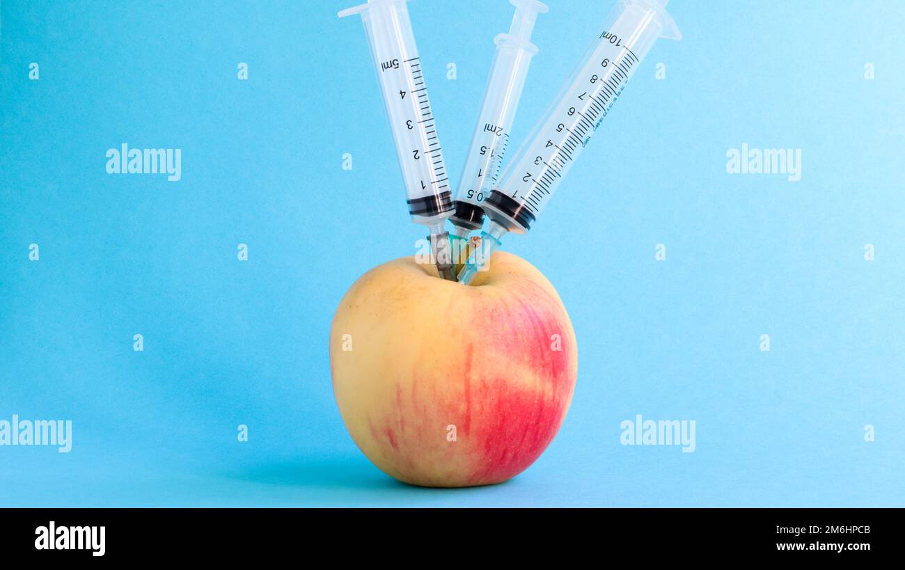 Tre diverse siringhe mediche che si attaccano in profondità in una mela su uno sfondo blu. Il frutto è cosparso di siringhe. Un rosso maturo Foto Stock