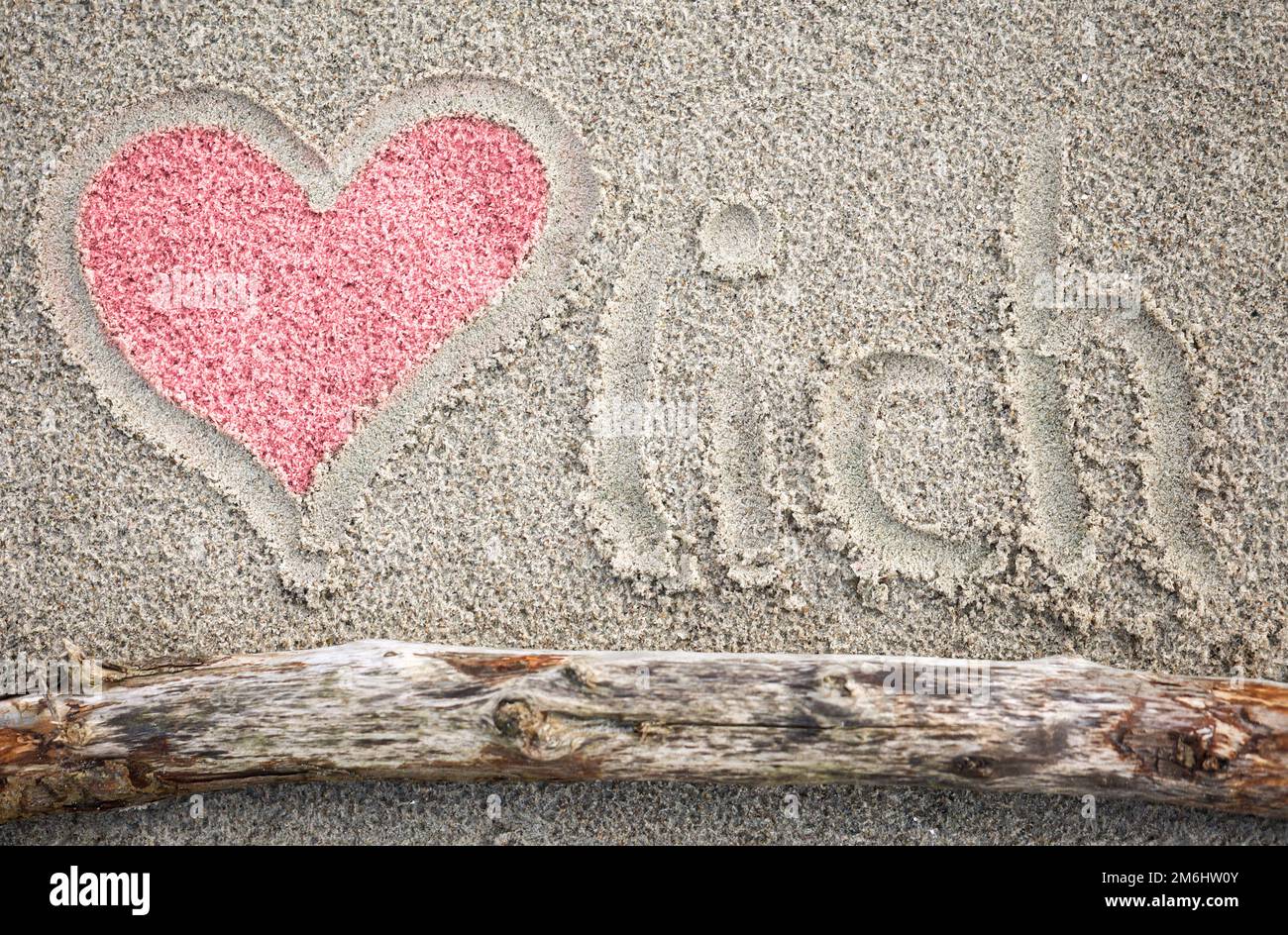 Un cuore disegnato nella sabbia, e la parola Herzlich. Foto Stock