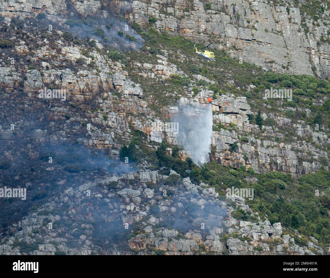 Un elicottero che scarica acqua per estinguere il fuoco selvaggio in montagna. Capo Occidentale, Sudafrica. Foto Stock
