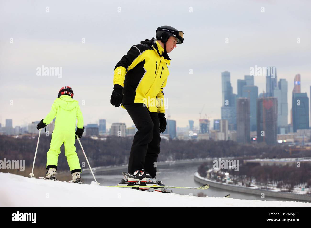 Sciatori uomo e bambino sullo sfondo dei grattacieli della città di Mosca. Persone sciare, divertimento in famiglia in inverno Foto Stock