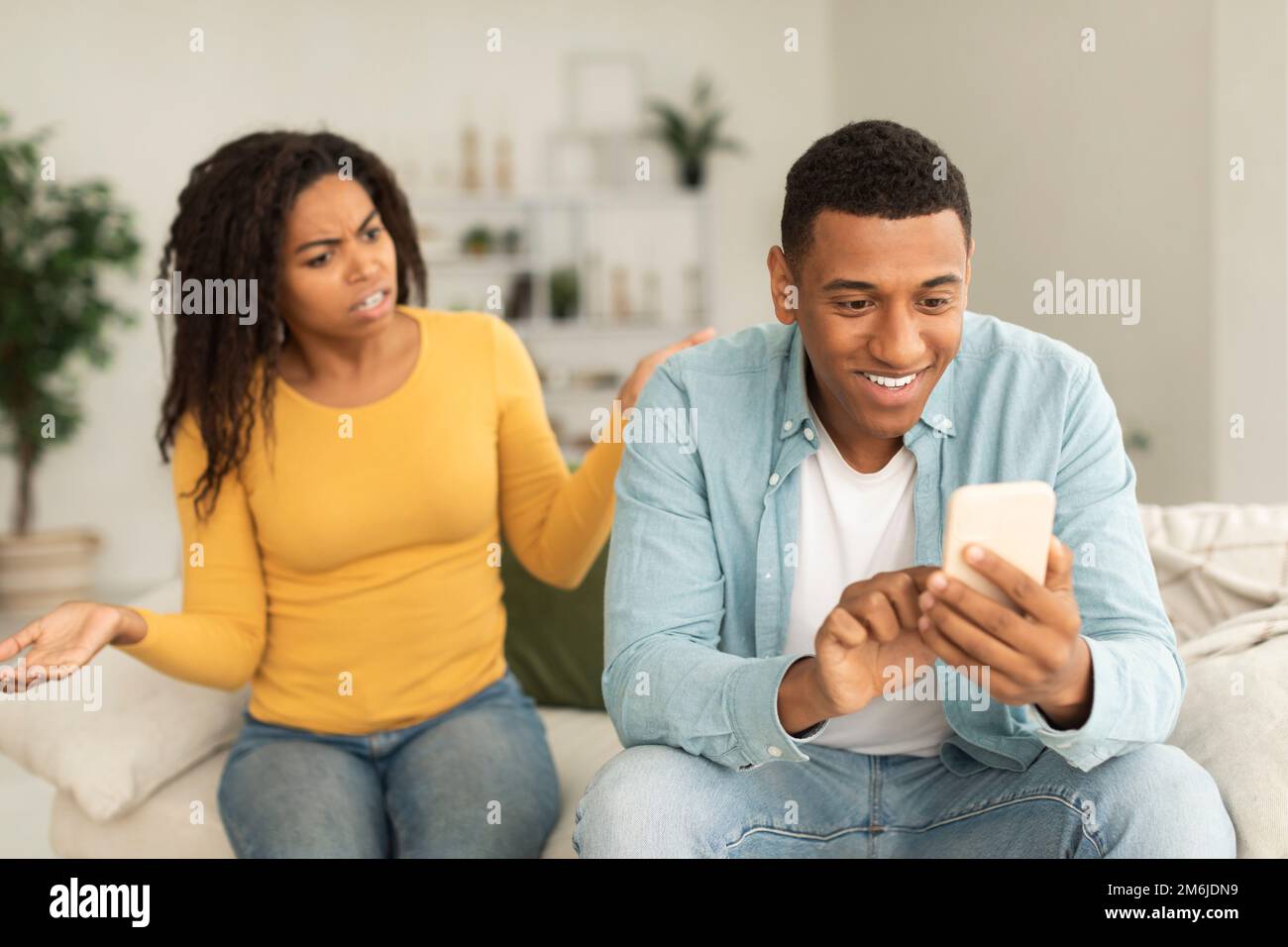 Arrabbiato offeso millenario afroamericana donna trasudare l'uomo con il telefono, soffre di dipendenza dai giochi Foto Stock