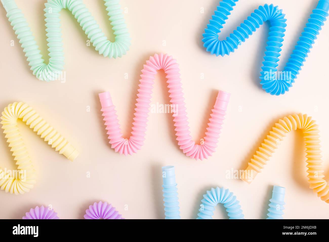 Giocattoli alla moda per bambini color pastello pop-tube su sfondo beige. Set di forme e colori corrugato tubo e anti-stress, relax Foto Stock
