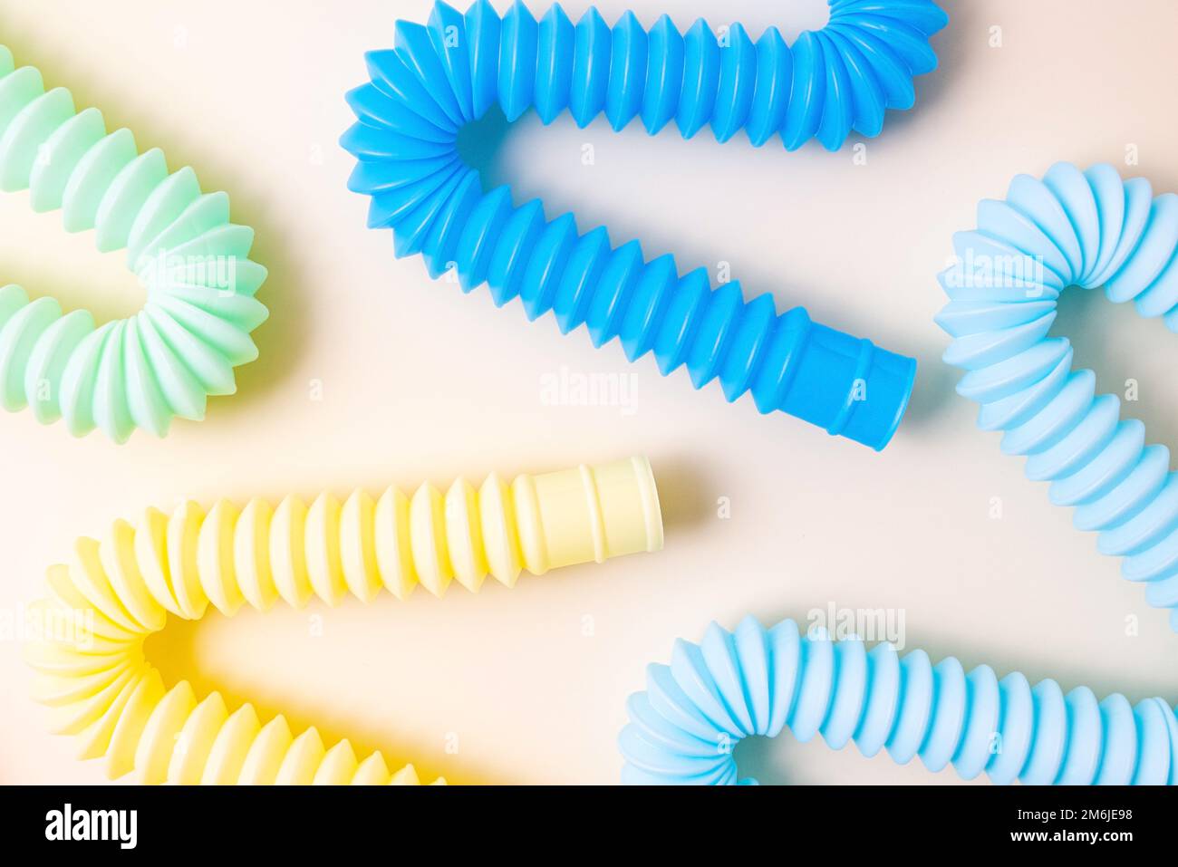 Giocattoli alla moda per bambini color pastello pop-tube su sfondo beige. Set di forme e colori corrugato tubo e anti-stress, relax Foto Stock