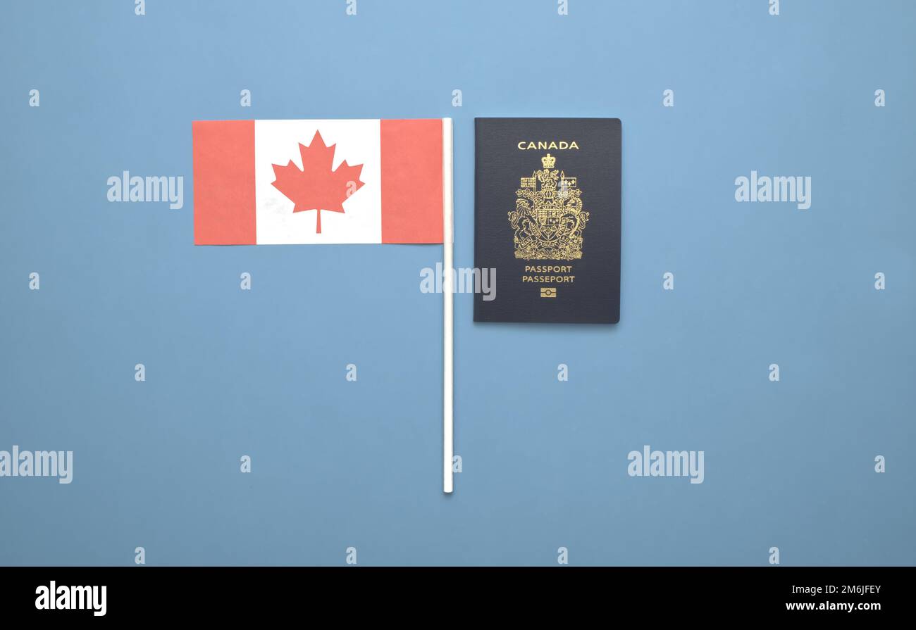 Un passaporto canadese accanto a una bandiera canadese su uno sfondo blu chiaro e solido Foto Stock