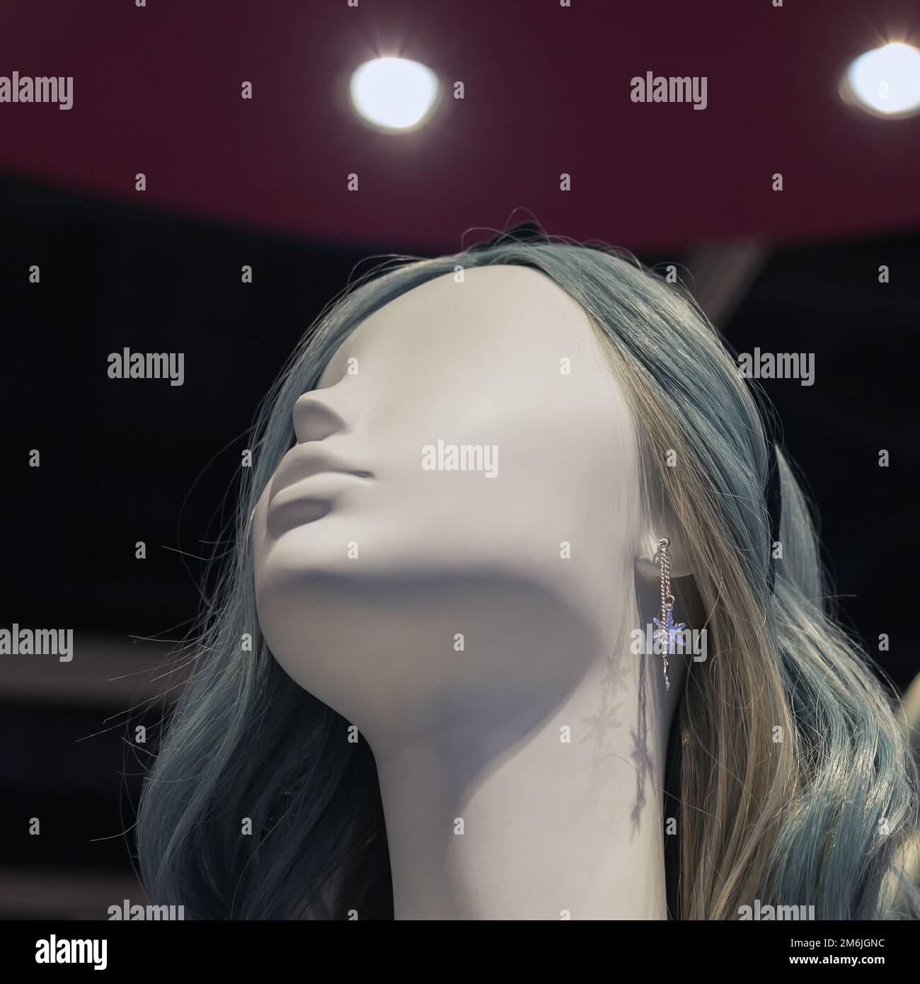 La testa di un manichino femmina bianco con capelli grigi e un orecchino in argento contro un soffitto viola con faretti. Panno alla moda Foto Stock