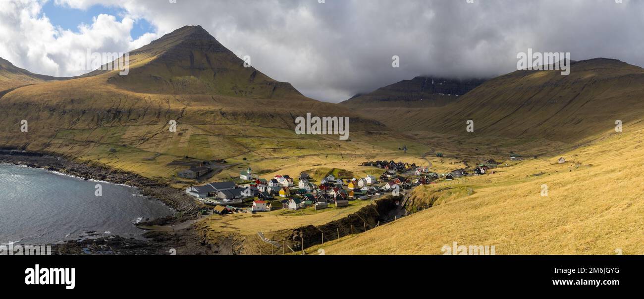 Villaggio di Gjógv sotto la montagna di Middagsfjall e la montagna di Slættaratindur coperta da nuvole Foto Stock