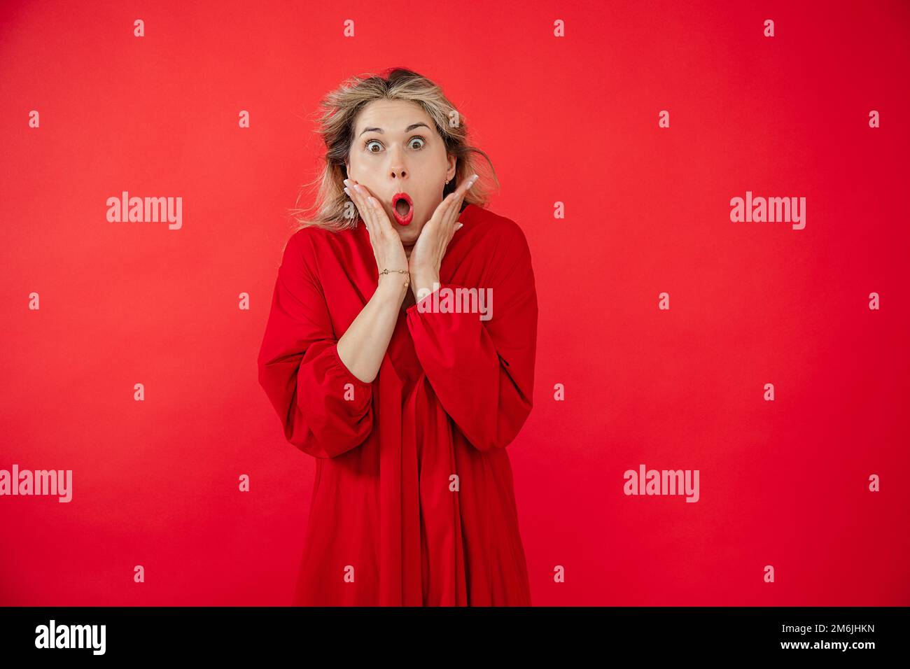 Ritratto di splendida giovane donna in abito rosso brillante che si chiedeva con la bocca aperta e gli occhi gonfie isolati su sfondo rosso. Effetto WOW, ottimo risultato Foto Stock