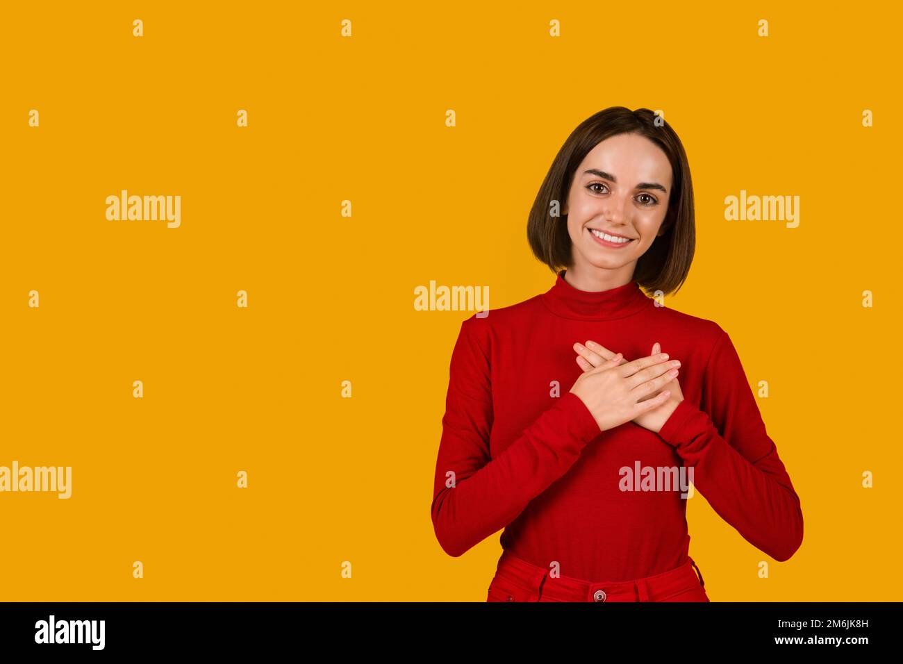 Giovane donna grata che tiene le mani sul petto Foto Stock