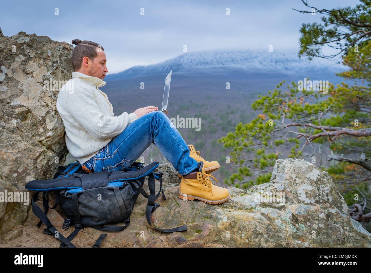 Uomo hipster che lavora con notebook seduto sulla montagna rocciosa su uno sfondo bellissimo scenica Clif Foto Stock