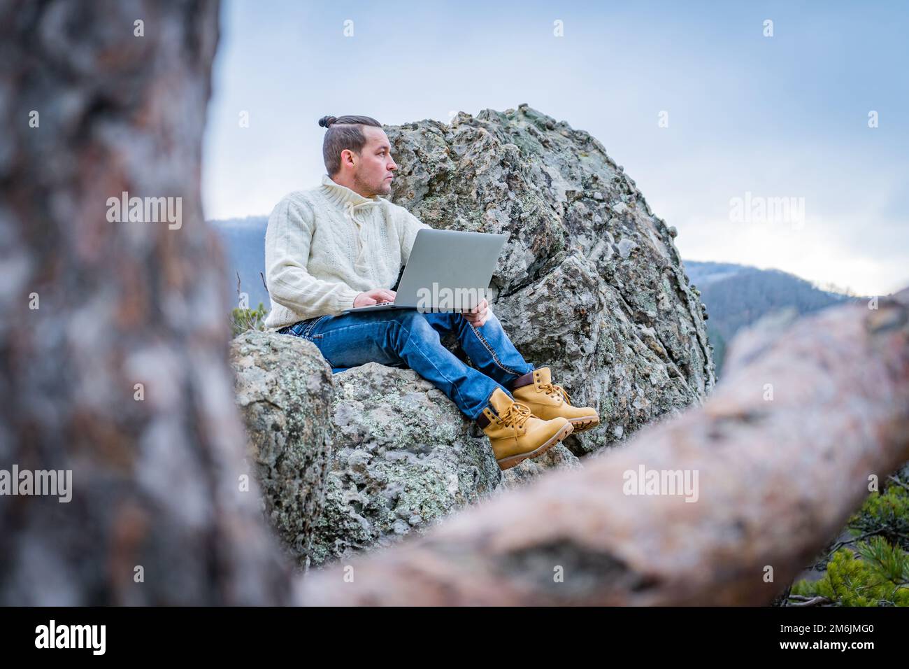 Uomo hipster che lavora con un computer portatile seduto sulla montagna rocciosa su uno splendido sfondo scenica della scogliera Foto Stock