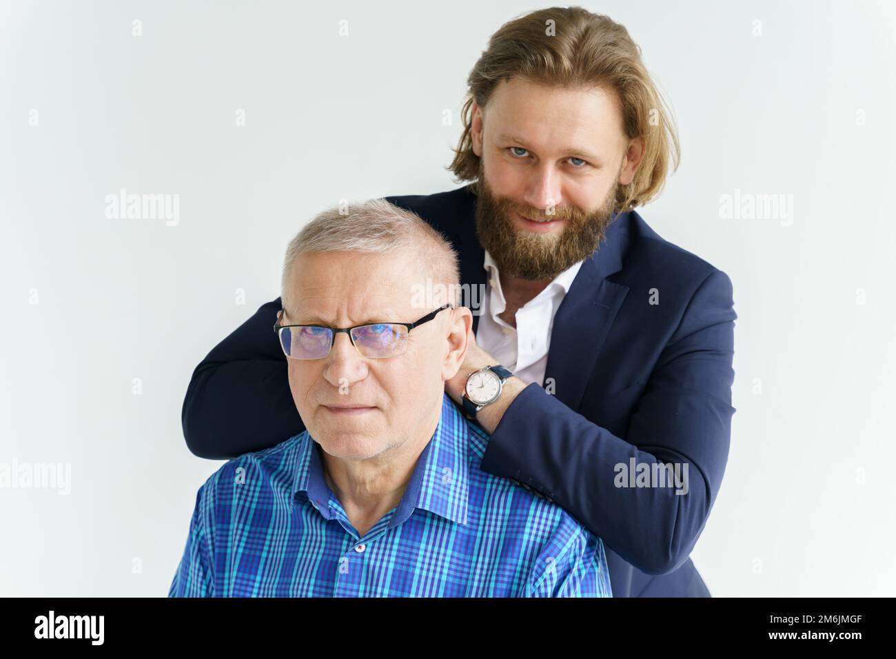 Il figlio in un abito elegante si appoggia sulle spalle del padre, Padre e figlio su sfondo bianco, entrambi gli uomini guardano nel camer Foto Stock Il figlio in un abito elegante si appoggia sulle spalle del padre, Padre e figlio su sfondo bianco, entrambi gli uomini guardano nel camer Foto Stock