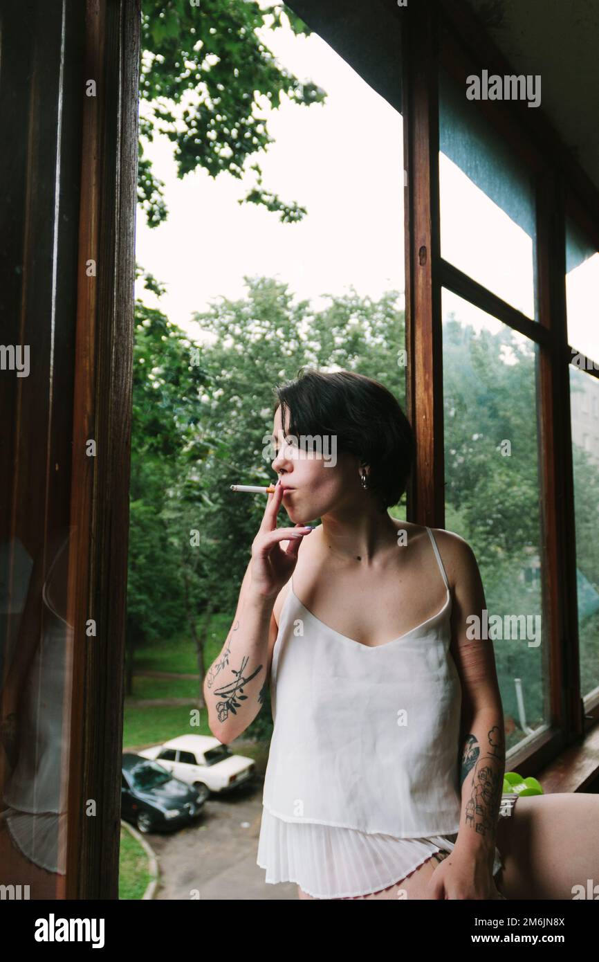 Donna con tatuaggi che fuma in piedi sul balcone Foto Stock