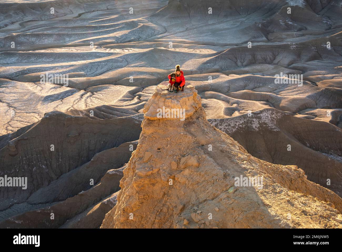Donna seduta con cane sulla formazione rocciosa nel deserto durante il tramonto Foto Stock