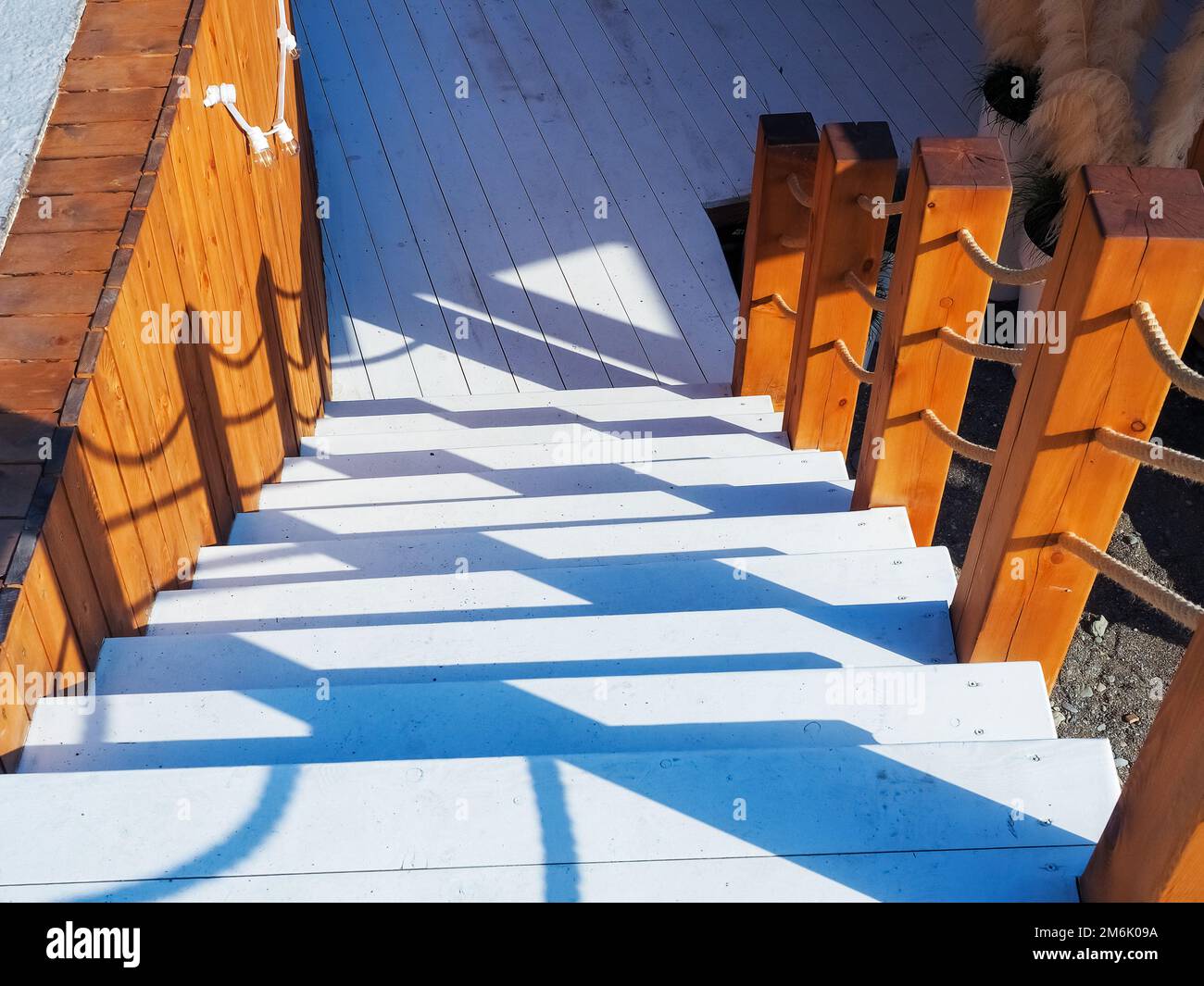 Scalini bianchi in legno con ringhiere decorative in stile nautico illuminate dal sole conducono ad un'area ombreggiata. Foto Stock