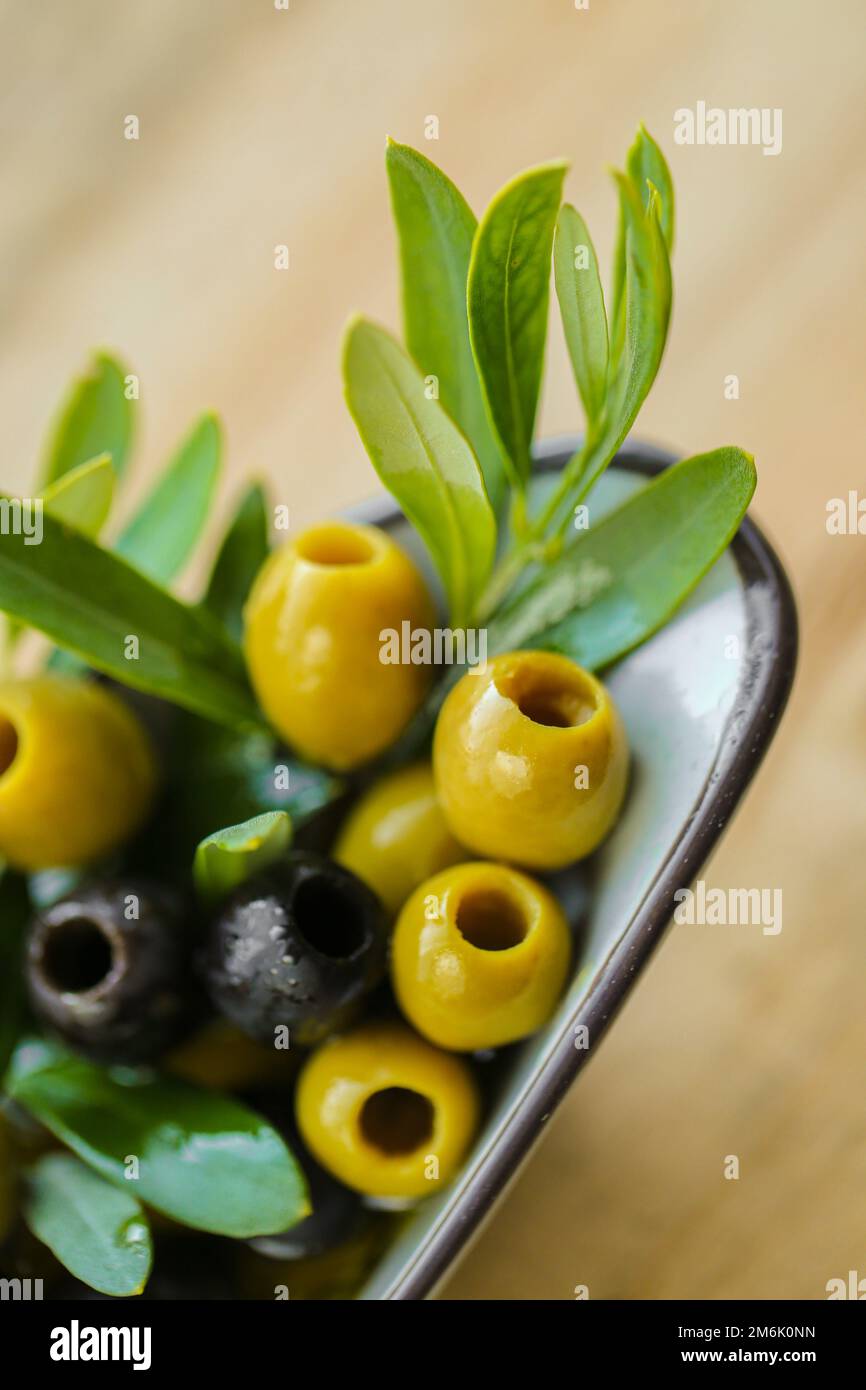 Olive e olio d'oliva. Ingrediente della cucina mediterranea. Olive nere e verdi e un ramo di olive verdi in olio d'oliva su un tavolo di legno. Foto Stock