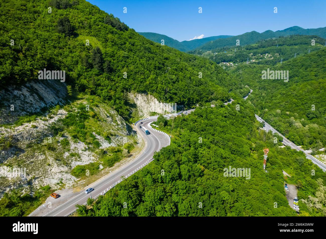 La strada asfaltata è immersa tra il mare blu e le verdi montagne. Veduta aerea dell'auto che percorre la tortuosa strada di montagna in S Foto Stock