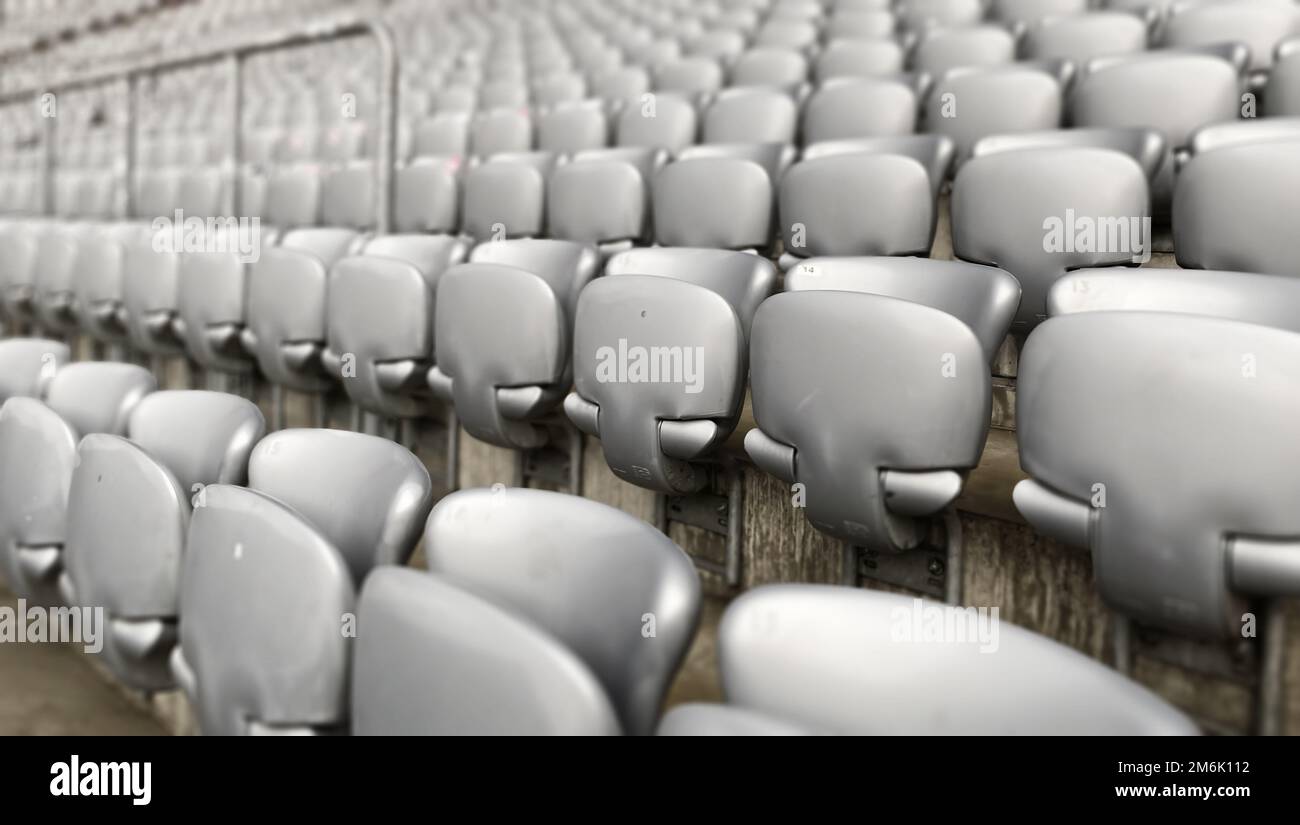 Sedie grigie vuote all'interno di uno stadio. Sedili in plastica disposti in file. Ripetizione e simmetria. Foto Stock