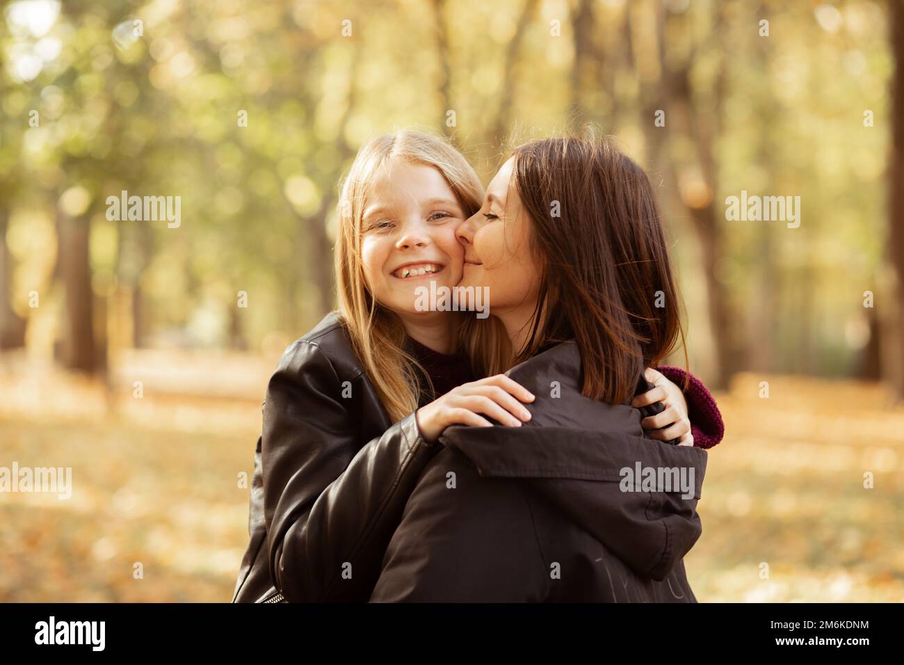 Ritratto di famiglia di giovane donna e ragazza adolescente che cammina nella foresta. Madre che tiene la figlia tra le braccia, baciando la guancia. Foto Stock