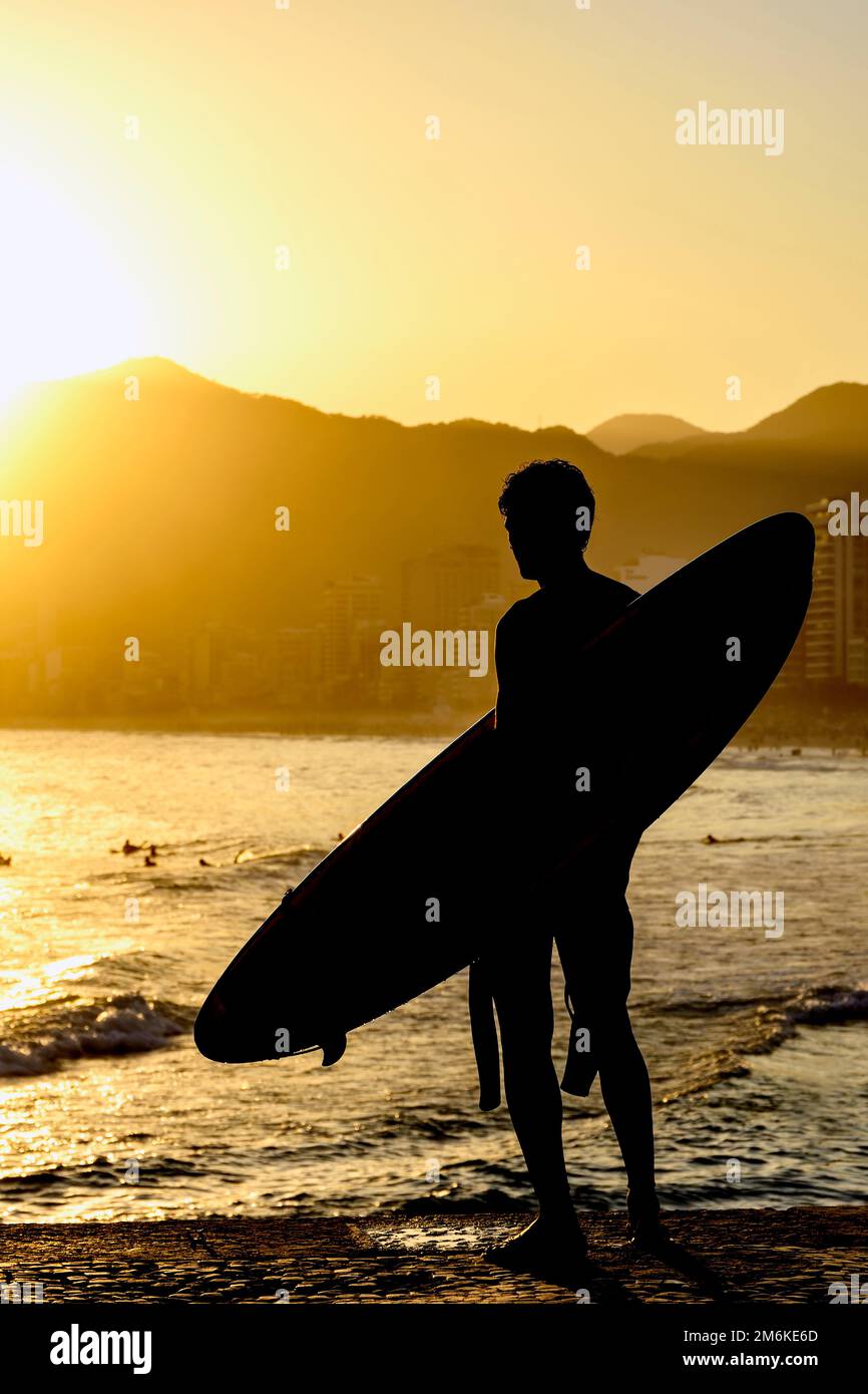 Surfista di fronte al mare che guarda le onde al crepuscolo Foto Stock