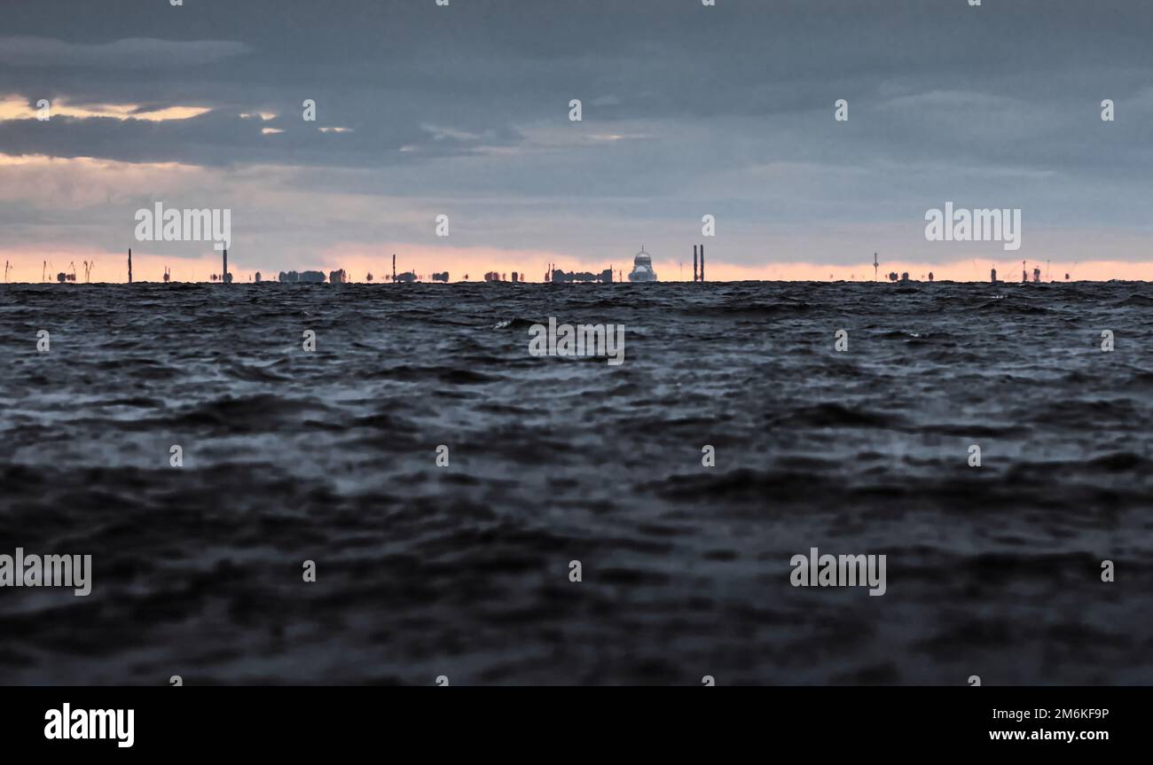 La città di Kronstadt all'orizzonte del mare in tempo nuvoloso, i contorni della città sono sfocati dal calore dell'acqua, tal Foto Stock