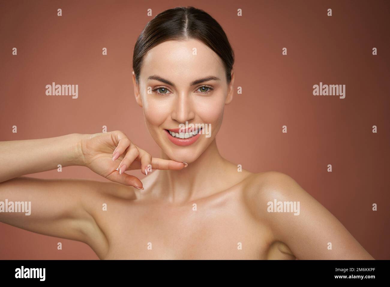 Donna sorridente che tocca la pelle contro il marrone Foto Stock