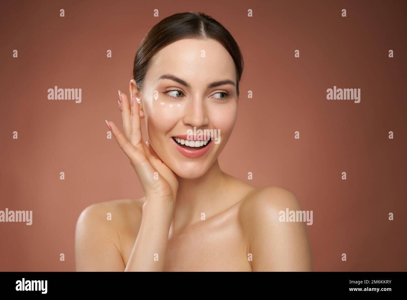 Donna sorridente che applica la crema sul viso Foto Stock