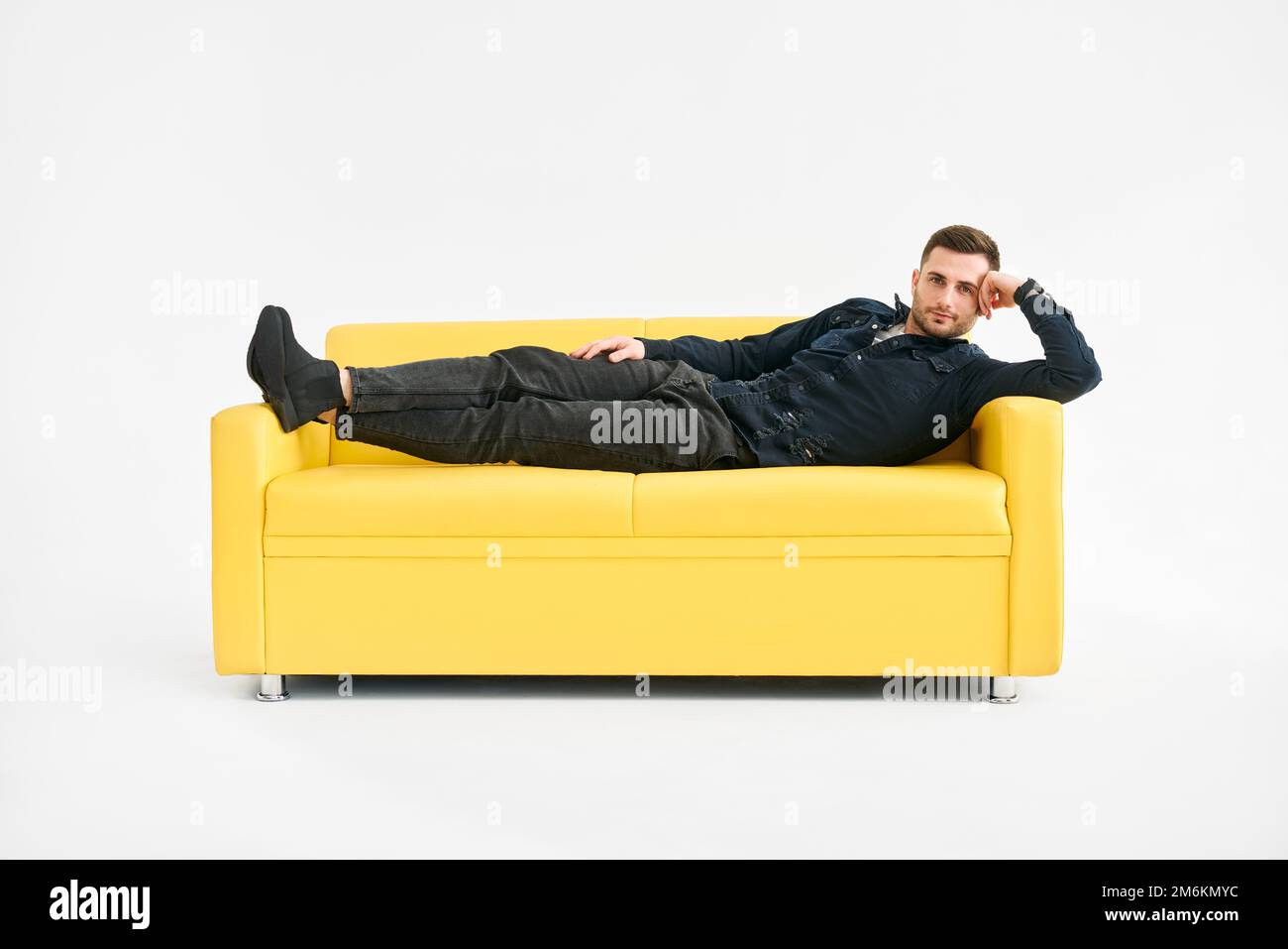 Giovane uomo che si rilassa da solo sul divano giallo a casa Foto Stock