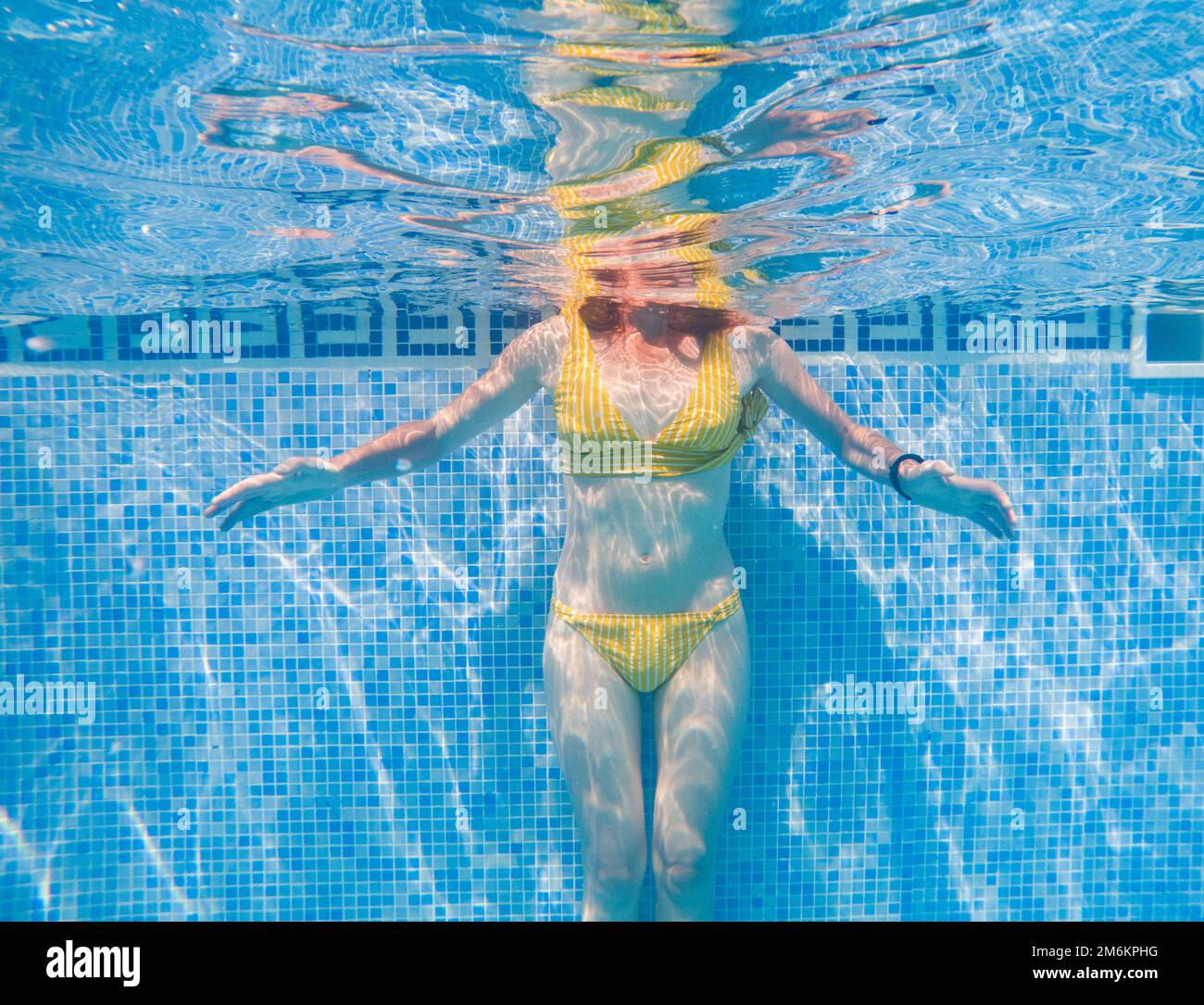 Donna in costume da bagno giallo in acqua blu chiaro in piscina Foto Stock