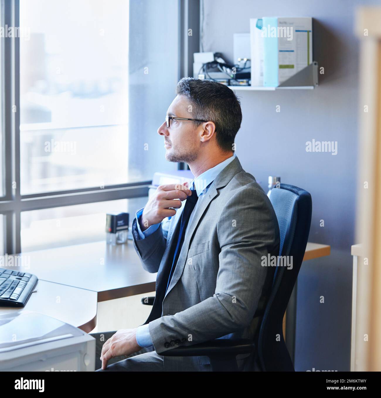 Preparazione per la revisione delle prestazioni. un uomo d'affari che aggiusta la cravatta mentre si siede alla sua scrivania. Foto Stock