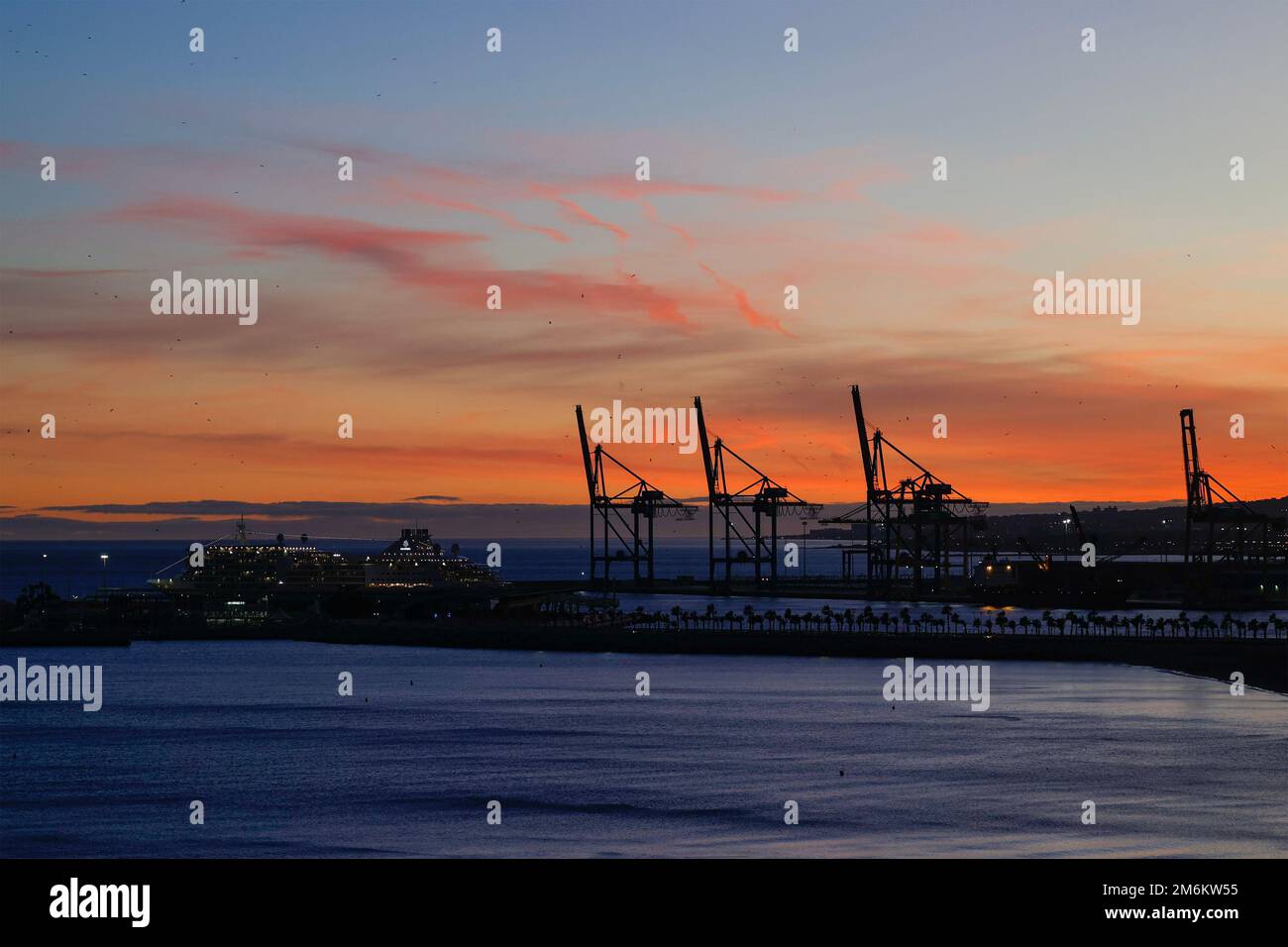 Vista tramonto con silhouette di gru industriali nel porto di Malaga, Andalusia, Spagna. Foto Stock