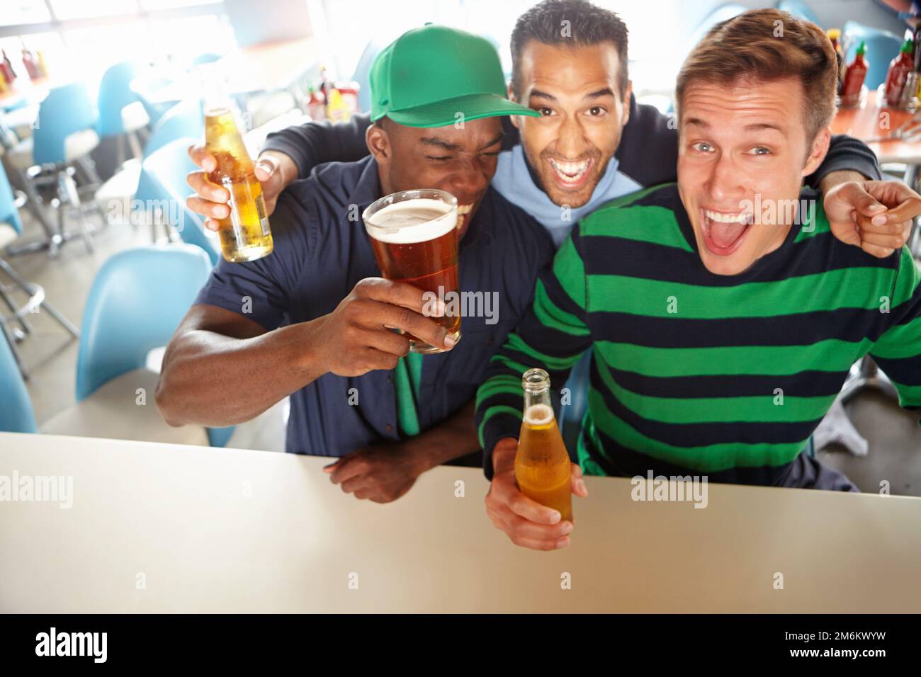 Questi ragazzi li stanno affondando indietro rapidamente. Vista dall'alto di tre amici che si rilassano al bar con birra. Foto Stock