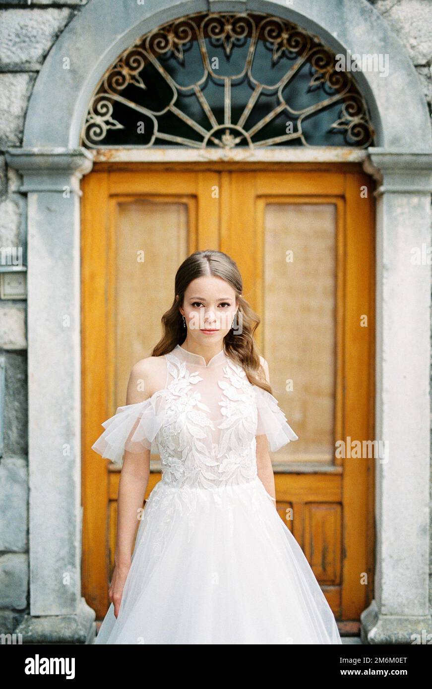 Sposa in un abito bianco si erge di fronte ad una porta di legno di un edificio in pietra Foto Stock