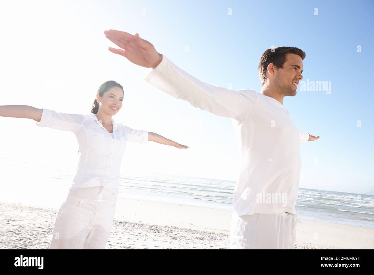 Trovare l'equilibrio di vita. un giovane uomo e una donna che fanno yoga al mare. Foto Stock