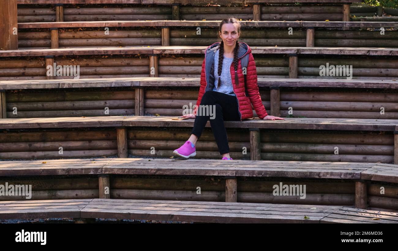 Giovane donna teen posti a sedere pubblico teatro all'aperto panchine in legno parco cittadino Foto Stock