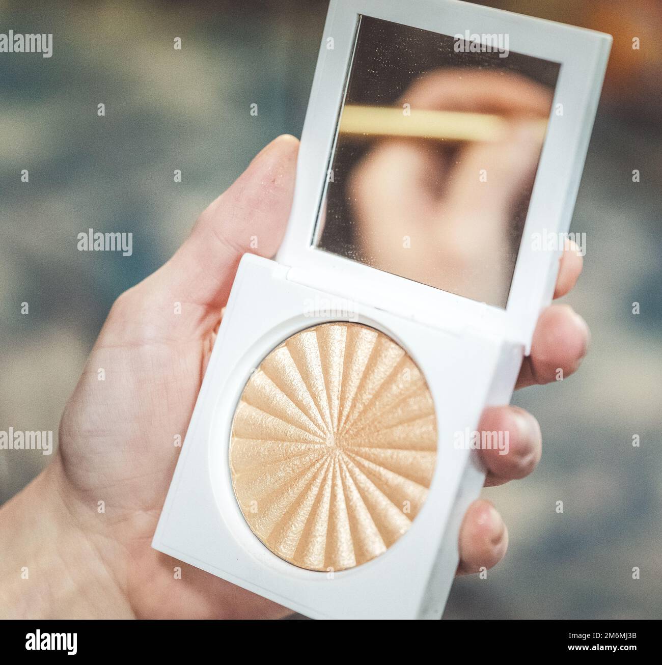 una mano che tiene un compattatore per il trucco con un riflesso dell'altra mano nello specchio Foto Stock