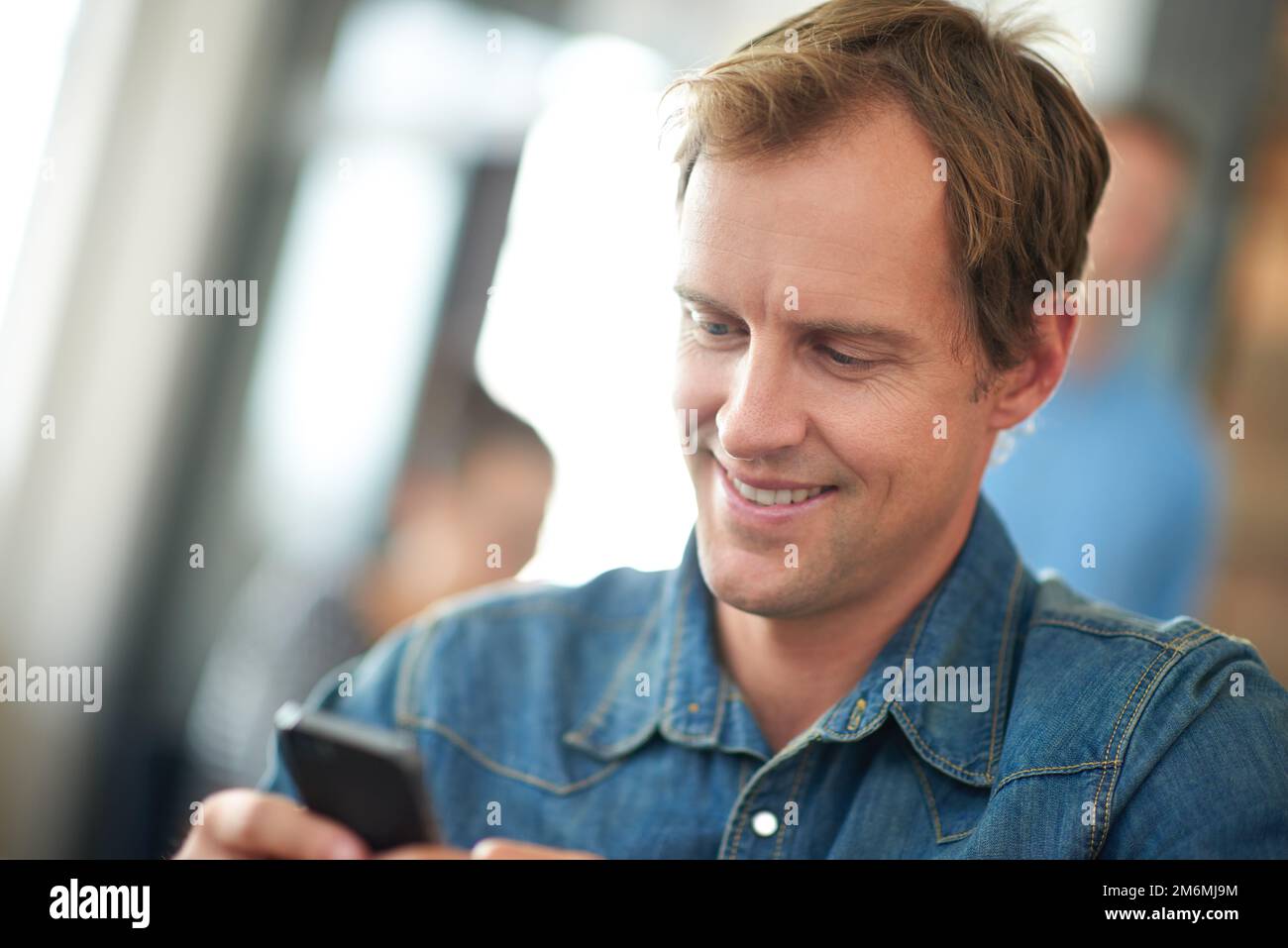 Organizzazione nel business di oggi. un uomo seduto in un ufficio messaggi su un cellulare con i colleghi in background. Foto Stock