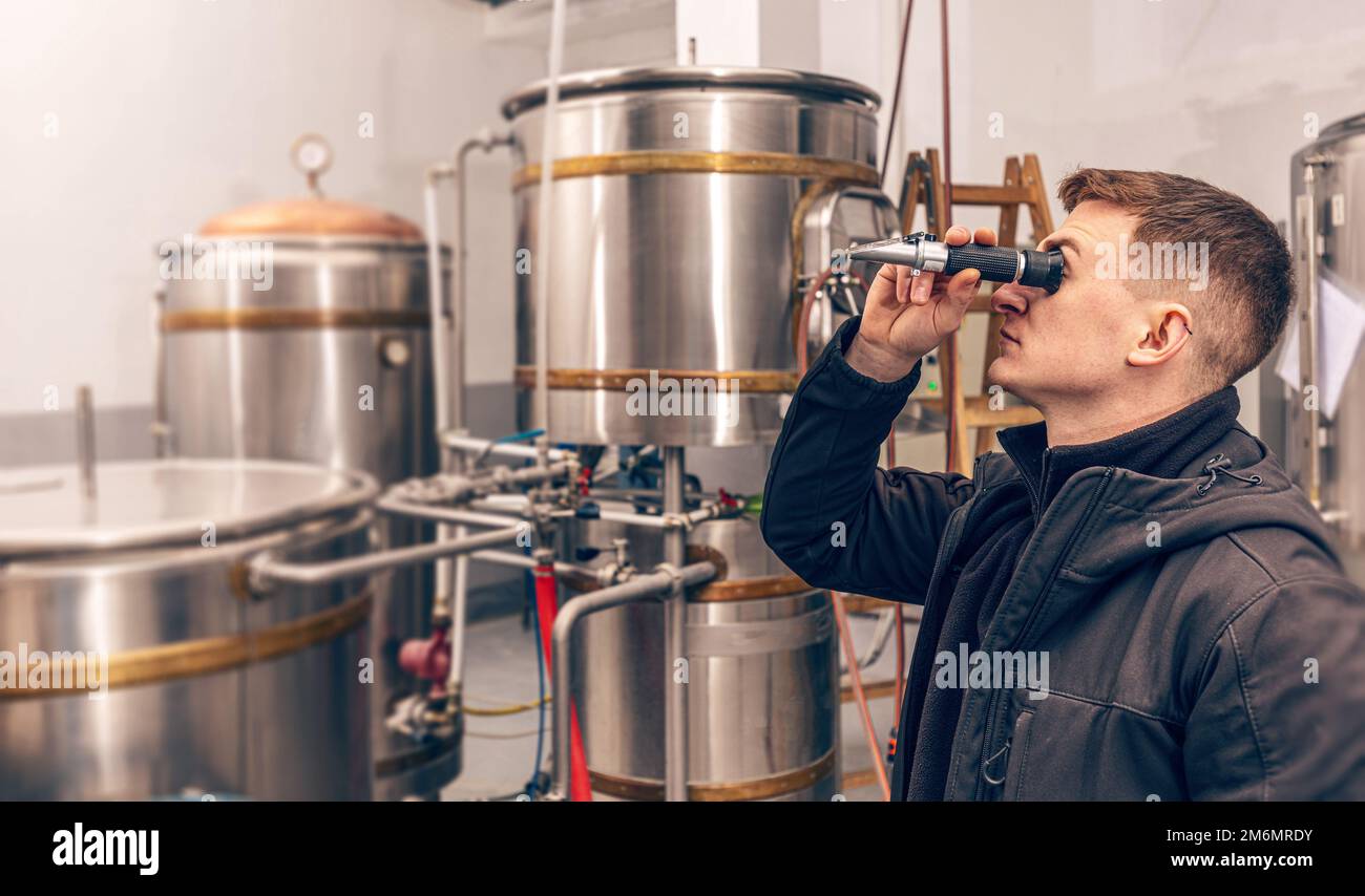 L'uomo guarda il rifrattometro per determinare il contenuto di zucchero della birra Foto Stock