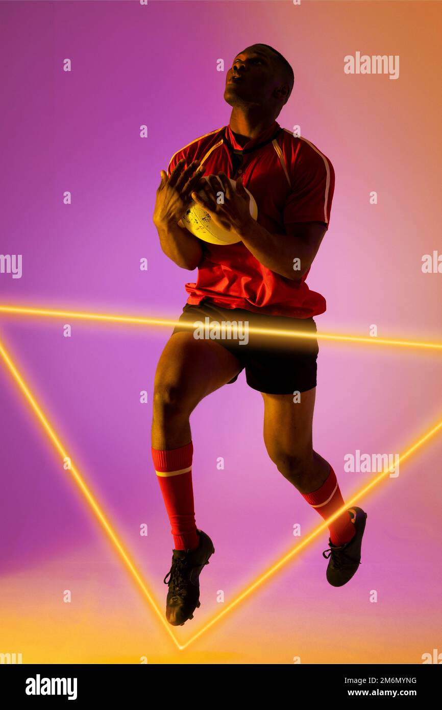 Lunghezza intera del giocatore di rugby maschio afroamericano che cattura il pallone e che salta dal triangolo illuminato Foto Stock