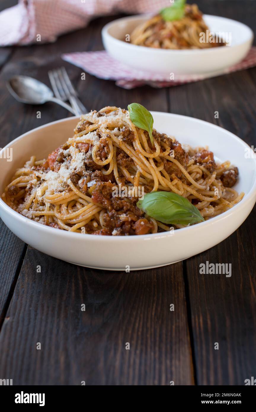 Spaghetti alla bolognese con parmigiano e foglia di basilico su un piatto su tavolo di legno con spazio per il testo. Cucina tradizionale italiana Foto Stock