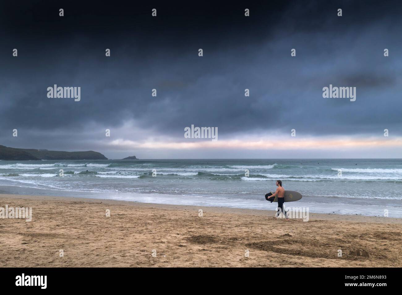Tempo del Regno Unito; nuvole di pioggia oscure e minacciose che si avvicinano come un surfista cammina lungo portare la sua tavola da surf a Fistral Beach a Newquay in Cornovaglia in Inghilterra in Foto Stock