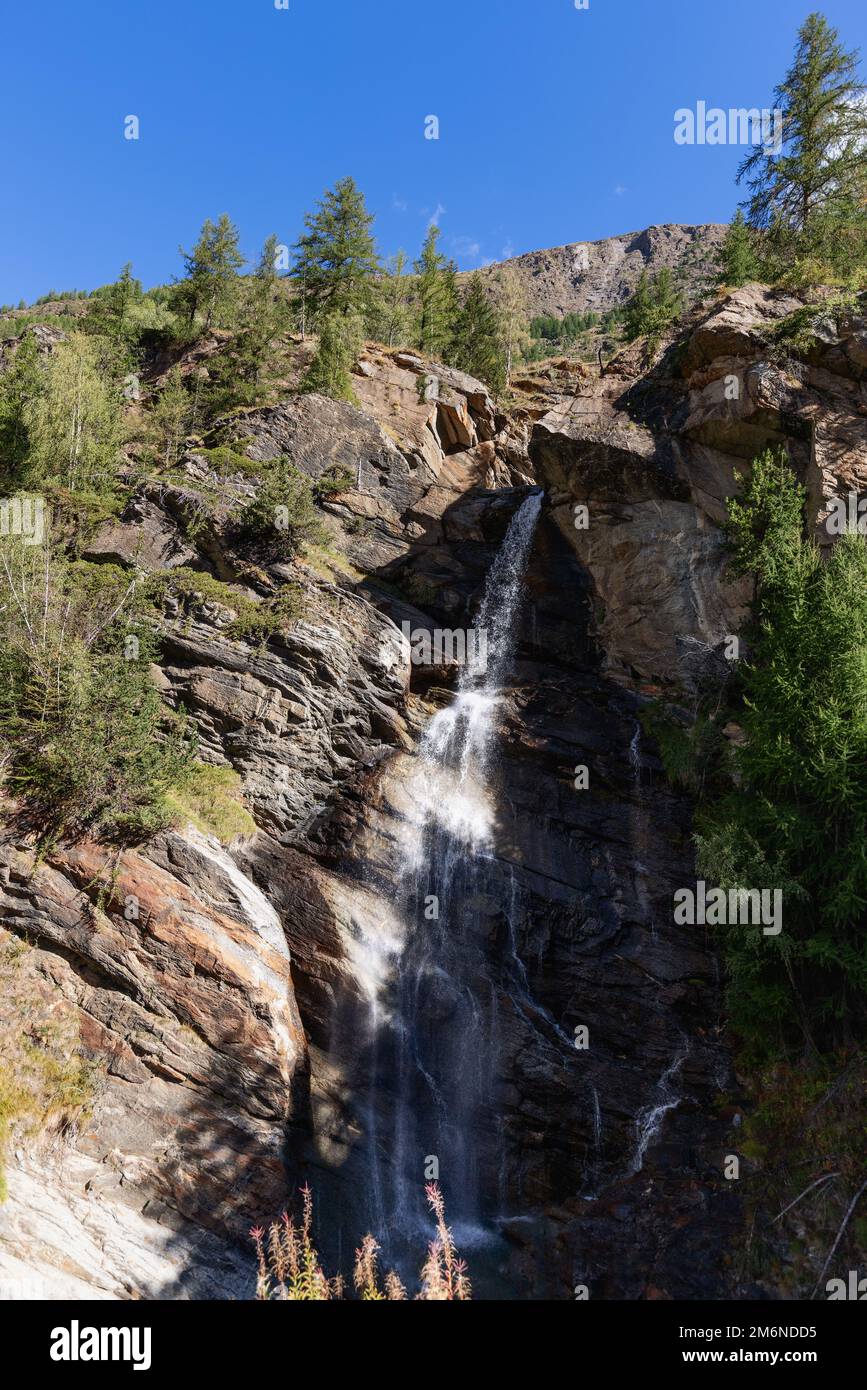 Ripido pendio con la cascata alpina di Lillaz (Cascate di Lillaz) in fessure di granito e alberi sottili in difetto contro il cielo blu. Valle d'Aosta Foto Stock