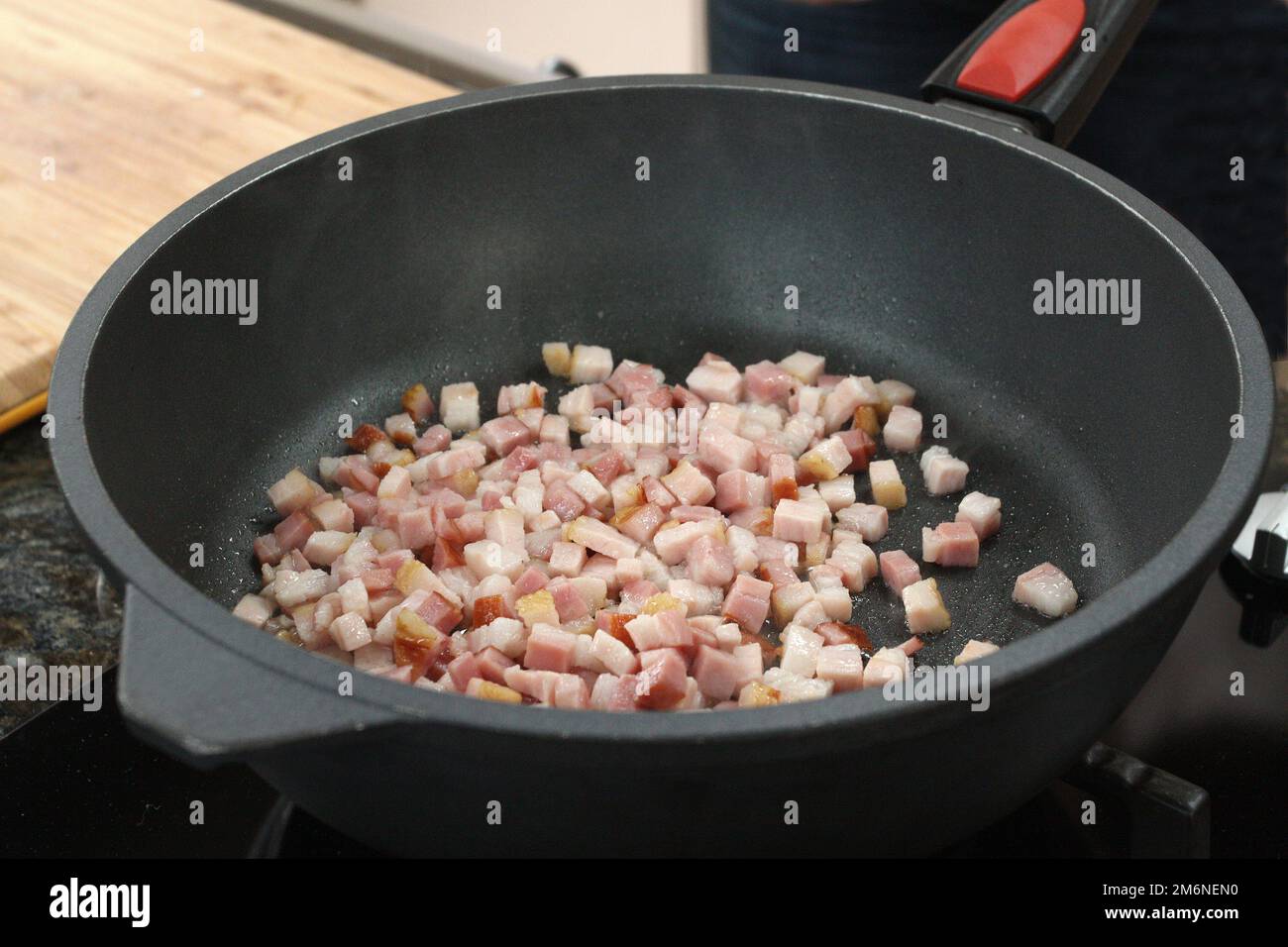 Pancetta cruda affettata che friggerà nella padella per preparare i greaves. Foto Stock