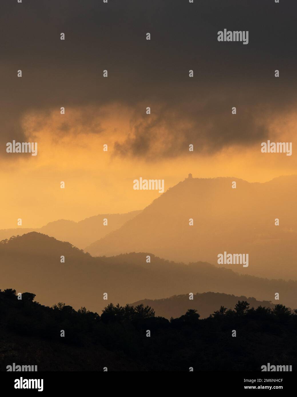 Tramonto con cielo nuvoloso e suggestiva luce del sole arancione sopra le vette delle montagne Foto Stock