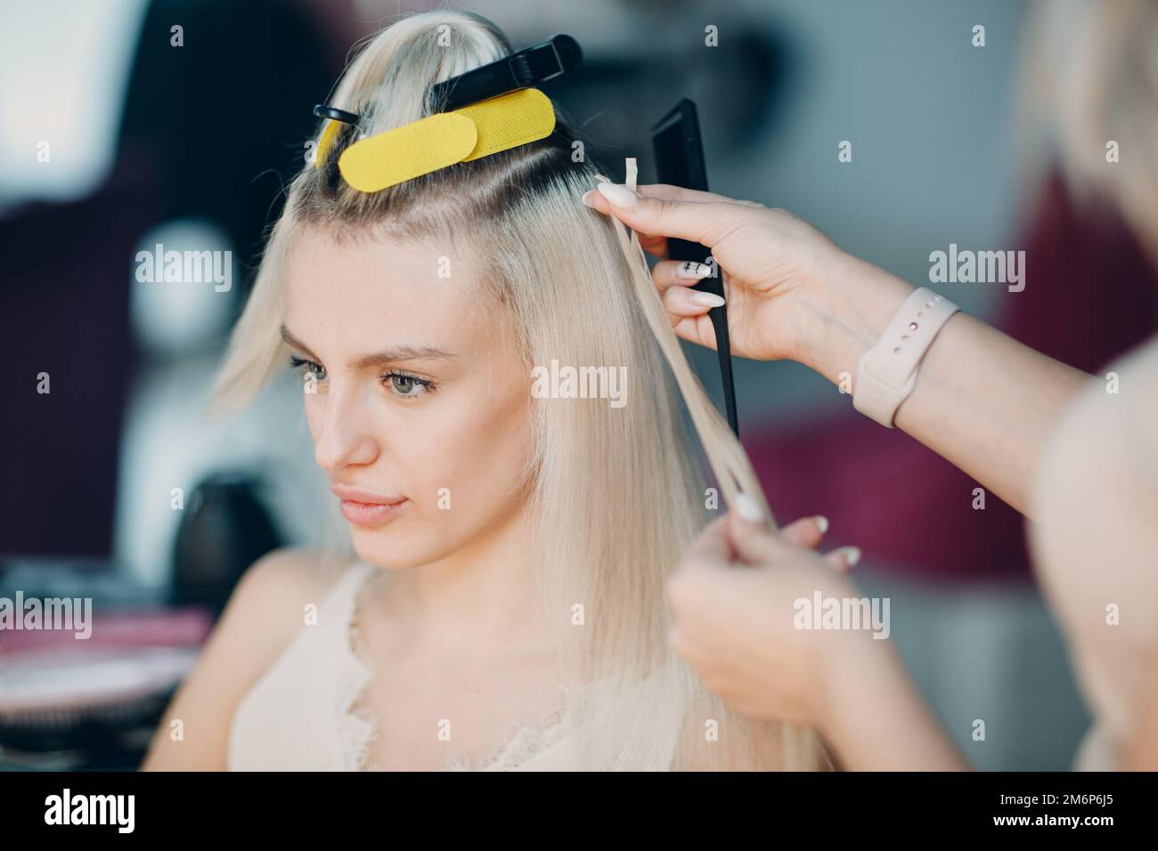 Parrucchiere femmina che fa estensioni di capelli a giovane donna con capelli biondi in salone di bellezza. Prolunga professionale per capelli. Foto Stock