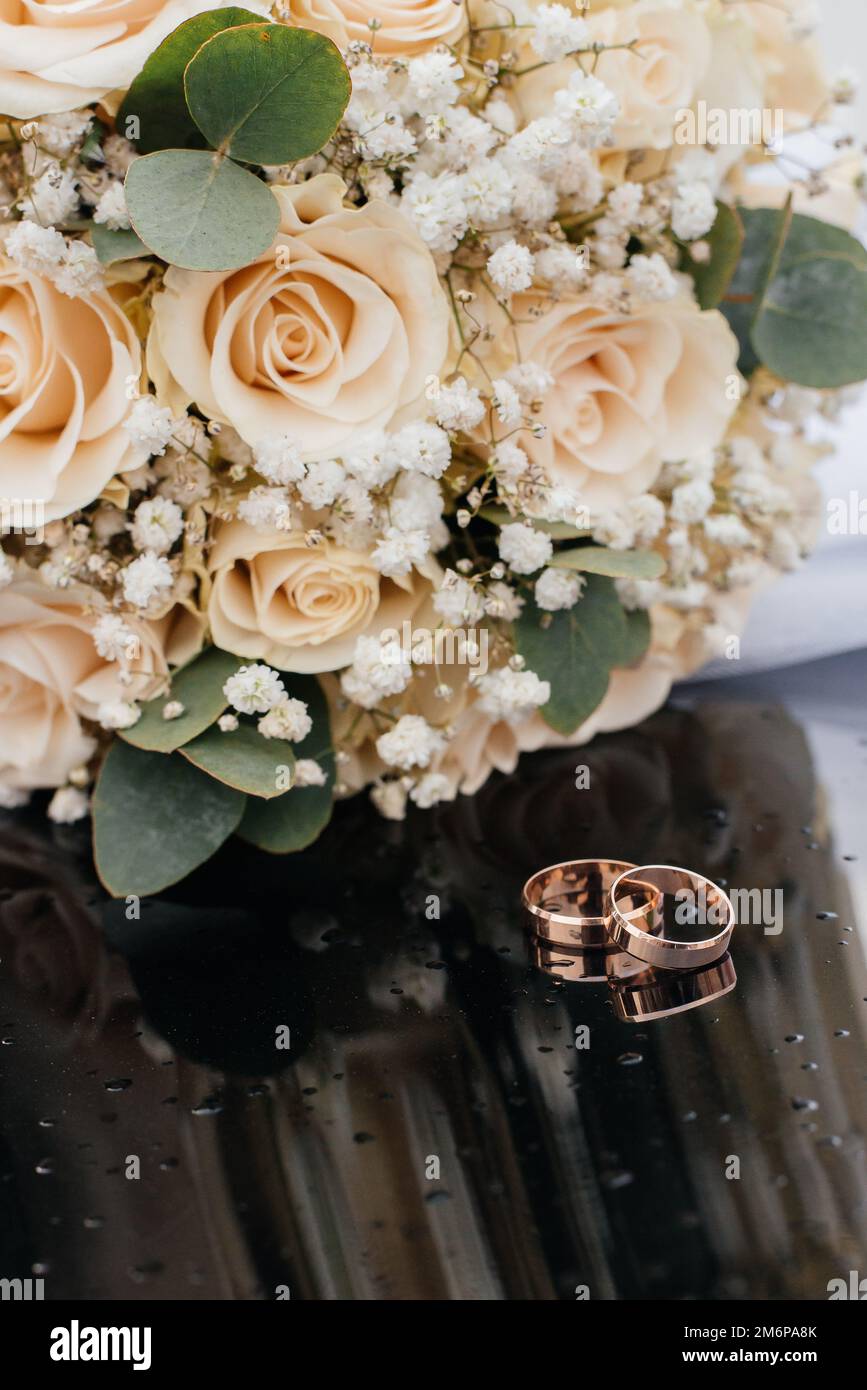 Una bella immagine dai toni con gli anelli di nozze si trova su una superficie nera contro lo sfondo di un bouquet di fiori Foto Stock