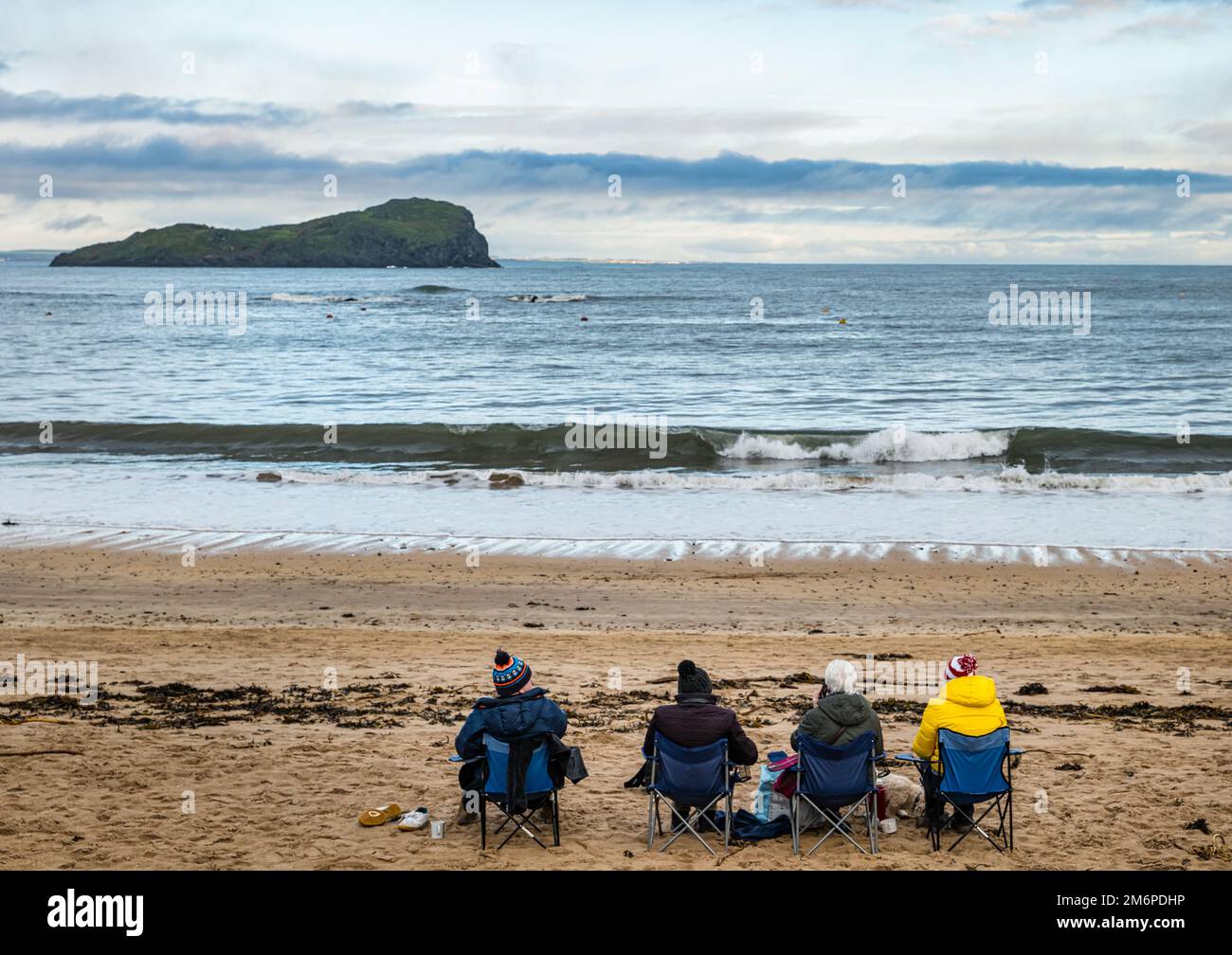 Persone che hanno un pic-nic sulla spiaggia seduti in sedie pieghevoli a basse temperature, Firth of Forth, North Berwick, East Lothian, Scozia, REGNO UNITO Foto Stock